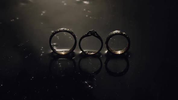 Wedding and Engagement Rings Lying on Dark Water Surface Shining with Light