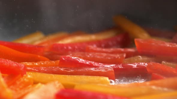 Camera tilting and shooting stir frying orange and red bell pepper . Slow Motion.