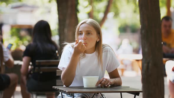 Young Girl is Having a Rest While Eating Delicious Ice Cream Sitting at Table in a Street Cafe