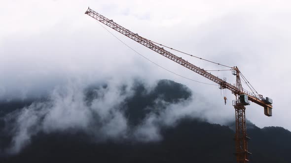 Construction site tower crane and flowing clouds over mountains background timelapse