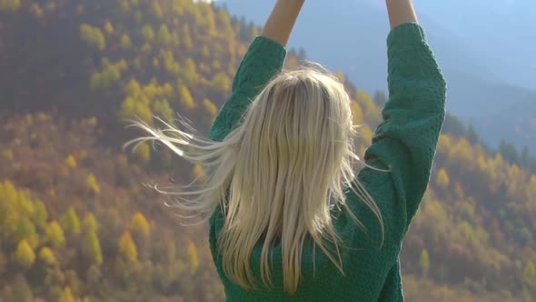woman straightens her hair and enjoys the nature of autumn mountain landscape.