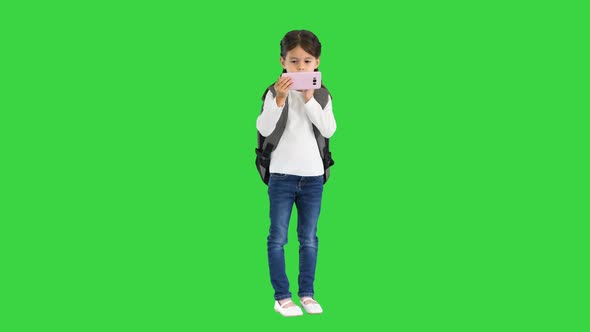 School Girl with Backpack Watching Something on Her Pink Phone on a Green Screen Chroma Key