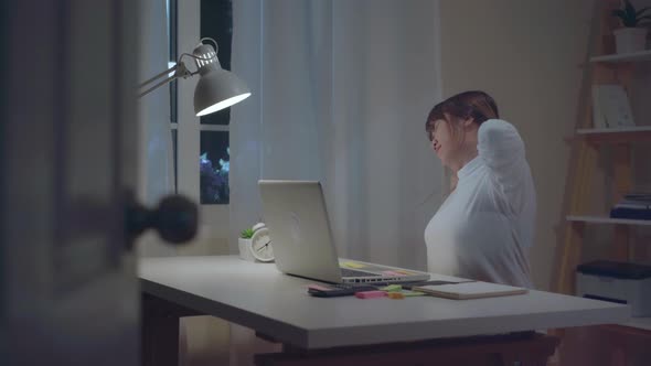 oung asian woman working late using laptop on desk writing notebook document sick and tired.