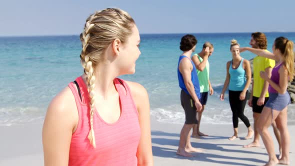 Fit woman smiling at camera while friends interacting behind her at beach