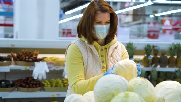 Shopper in medical mask picking cabbage at grocery store during pandemic