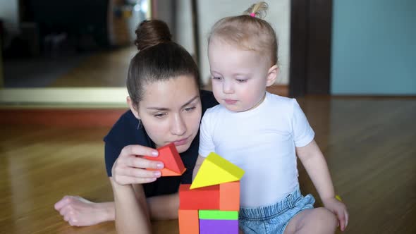 Mom with a small daughter build a tower of colored figures