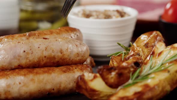 Taking Smoked Sausages with Fork Fried Potatoes and Sauce Closeup