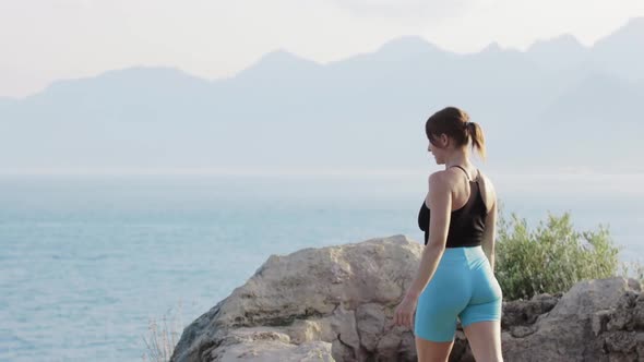 Sports Outdoors  a Fitness Woman Stands on the Rocks on the Hill and Looks at the Sea