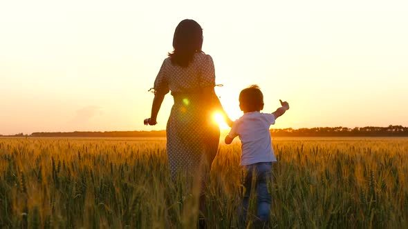 Silhouette of a Woman and a Child at Sunset. A Happy Mother Holds Her Son's Hand and They Run Across