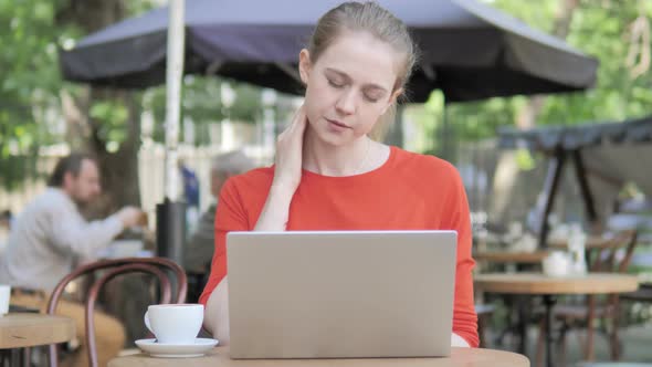 Young Woman with Neck Pain Using Laptop in Cafe Terrace