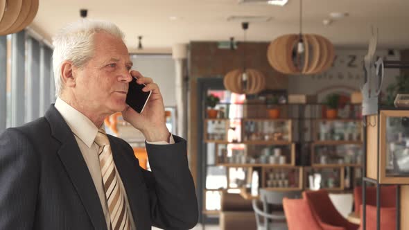 Senior Businessman Fininshes To Talk on the Phone at the Cafe