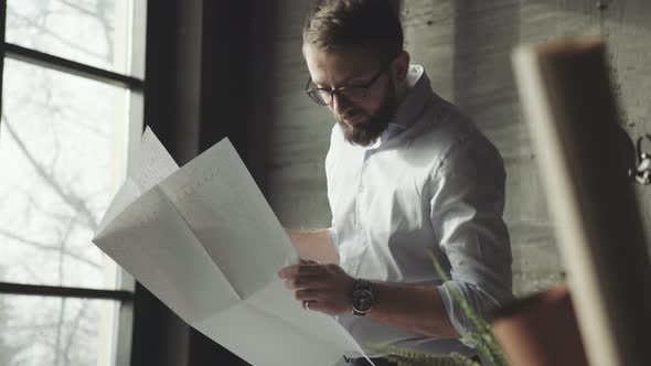 Architect with Beard, Glasses Works in Stylish Office with Blueprint