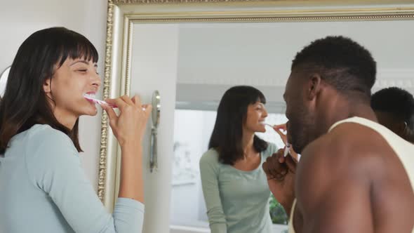 Happy diverse couple looking in mirror and brushing teeth in bathroom
