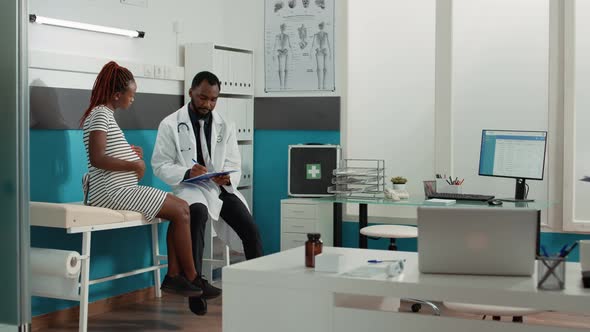 Male Physician Taking Notes at Checkup Visit with Pregnant Woman