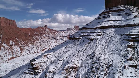 Flying past snow covered desert mesa revealing Castleton Tower