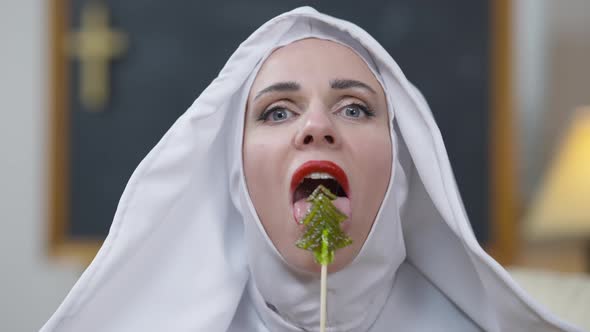 Headshot of Provocative Seductive Beautiful Woman in Nun Costume Licking Lollipop Smiling Looking at