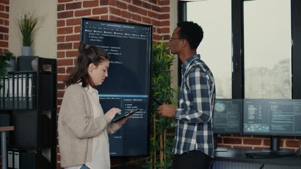 Software Developers Analyzing Source Code on Wall Screen Tv Comparing Errors Using Digital Tablet