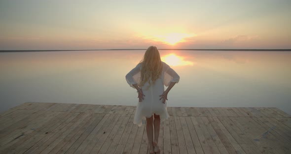 Woman with Blonde Hair is Dancing on the Pier of a Lake During Sunset