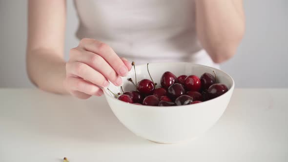 Young woman hands take delicious red cherry removes stem