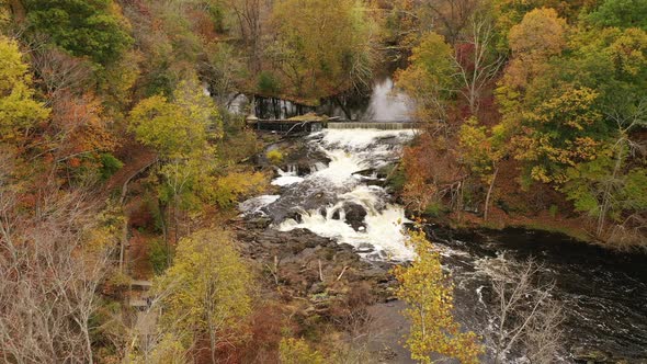 An aerial drone shot over the colorful fall foliage in upstate NY. The camera dolly out from a water