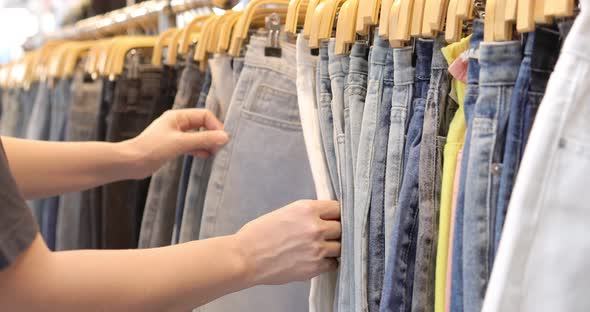 Close up woman hand choosing denim jeans hanging with rack in mall shop or cloth store.