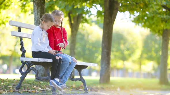 Little Adorable Girls with Smartphone in Fall Outdoors. Kids Having Fun at Warm Sunny Day in Autumn