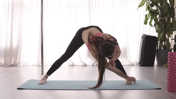 Young Graceful Girl Stretches the Muscles of the Arms and Legs on the Mat