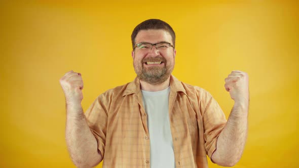 Joyful adult male in yellow shirt showing success gesture and smiling on camera satisfaction