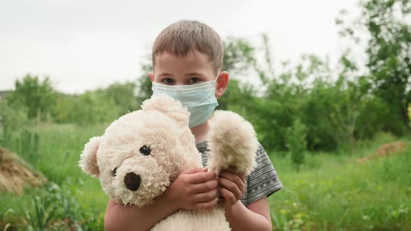 Little child in mask holding teddy bear and waving hand