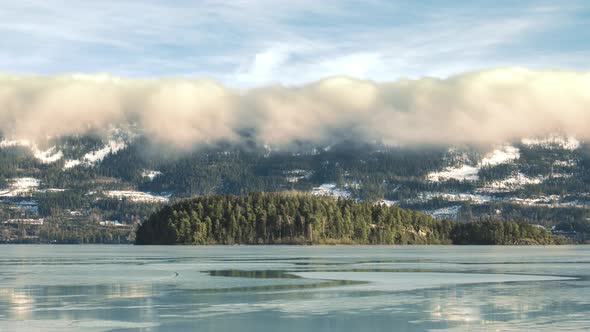 Clouds Moving On Top Of Lush Mountains In Staeinsfjorden, Norway With Icy Lake On Foreground In Wint