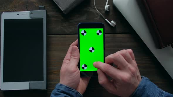 Hands of Man Using Smartphone  with Green Screen on Wood Table