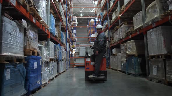 The Worker Rides Along the Row Along the High Racks with the Products