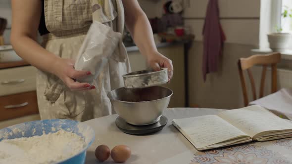 Close-up of bakery concept - Woman sift cocoa powder through metallic sieve to bowl for baking