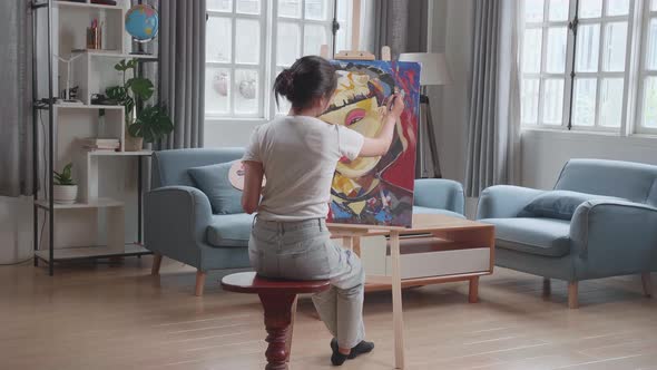 Hind View Of An Asian Artist Girl Holding Paintbrush Mixed Colour And Painting A Girl's Face