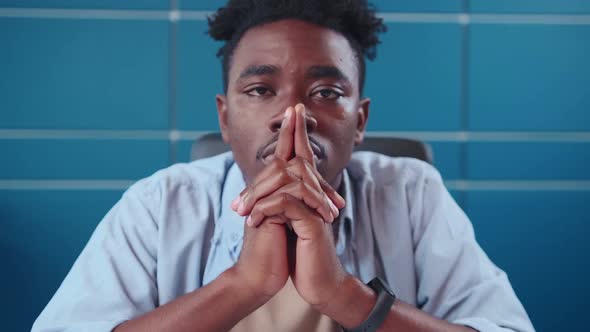 Young African American Man Stares Straight at your Sits at Working Table