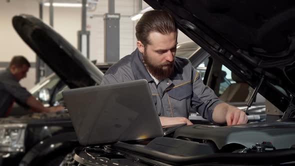 Car Service Worker Using Laptop Examining Engine of a Car