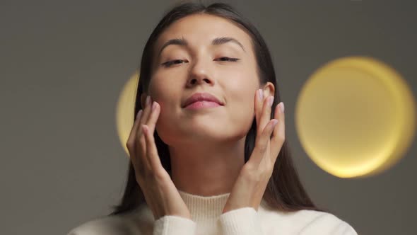 Portrait of a Beautiful Young Asian Woman Touching Her Perfect Skin and Looking Into the Camera