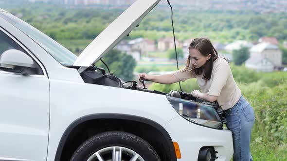 The woman pulls out a probe in her car engine to check the oil level.