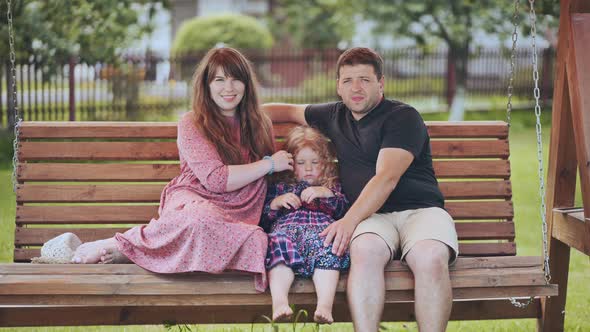 Portrait of a Young Family on a Swing in the Garden