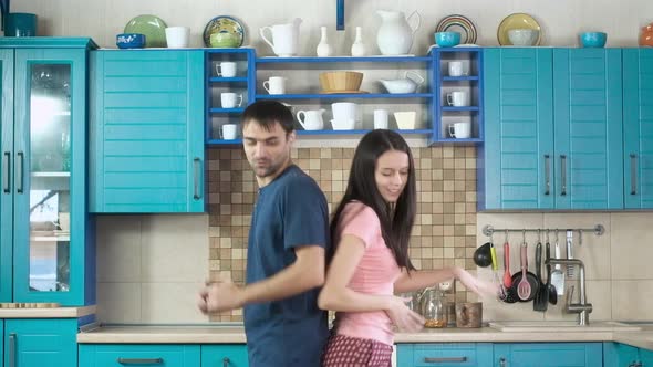 young man and attractive woman in colorful pajamas dancing in cozy kitchen.