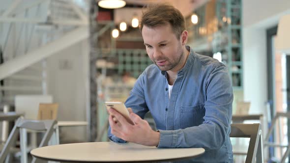 Serious Casual Man Using Smartphone in Cafe