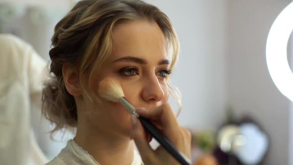 Close-up of make-up artist putting rouge on cheek of pretty woman using brush.