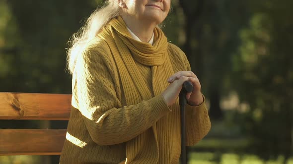 Happy Old Woman Sitting With Walking Stick in Park, Social Care for Disabled