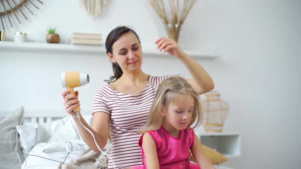 Young Woman Drying Hair To Her Daughter at Home