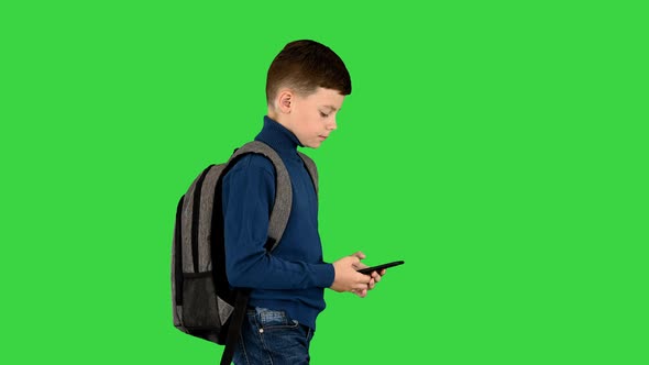 Schoolboy with a Backpack Using Mobile Phone While Walking on a Green Screen Chroma Key