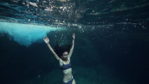 A Young Skinny Woman in Bikini Floating Underwater and Holding Her Breath