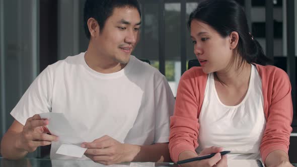 Young Asian Pregnant couple records of income and expenses at home happy using laptop record budget