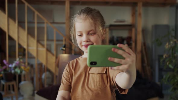 A Teenage Girl with Blond Hair Takes Pictures of Herself on a Mobile Phone