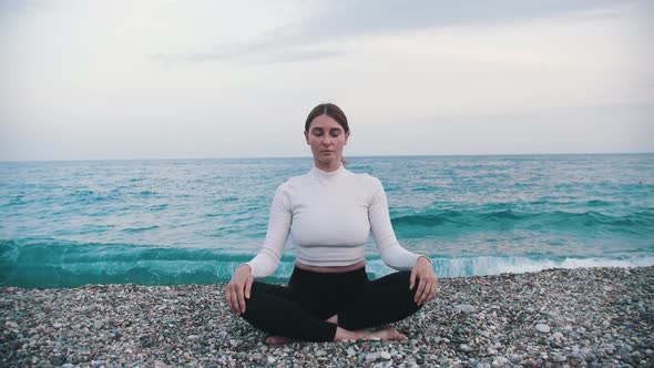 A Woman Sits on the Pebble Beach in the Lotus Position By the Blue Sea