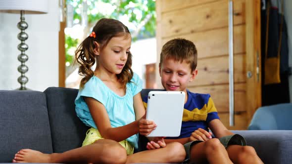 Siblings using digital tablet in living room alt